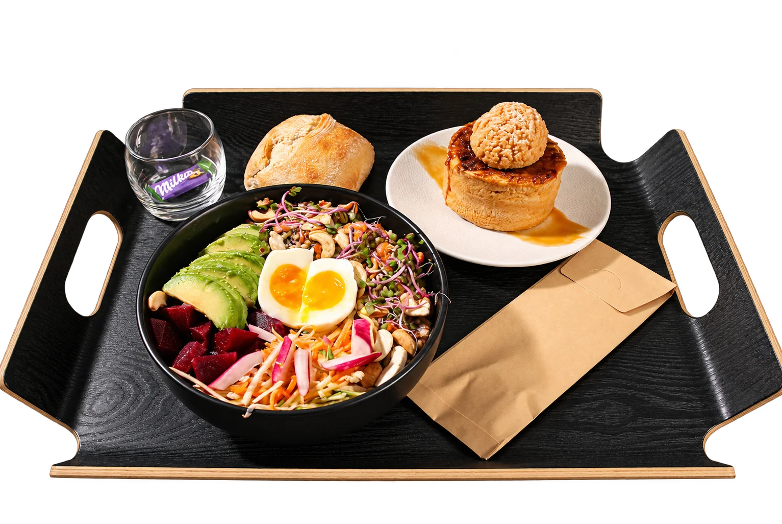 Un plateau noir présente un bol de salade avec avocat, betterave et œuf mollet, un petit pain, un dessert caramélisé sur assiette blanche et un verre contenant un chocolat Milka.